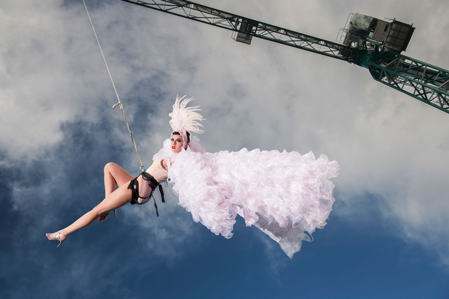 Fashion- und Lifestylebilder, Fashion-Fotos von Bevis, Fotograf in Kiel. Frau schwebt am Kran im weißen Kostüm im Himmel.